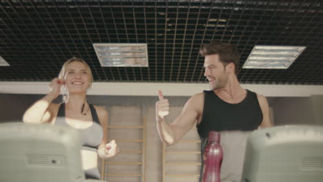 Joyful-fitness-couple-talking-on-treadmill-machine-in-gym-club.