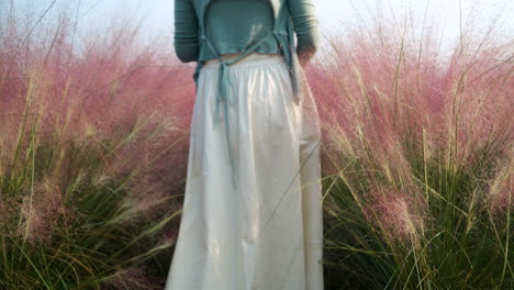 mujer en forma en vestido caminando a través de la hierba rosa muhly floreciente en la granja de la isla de hierbas - movimiento lento de ángulo bajo estático