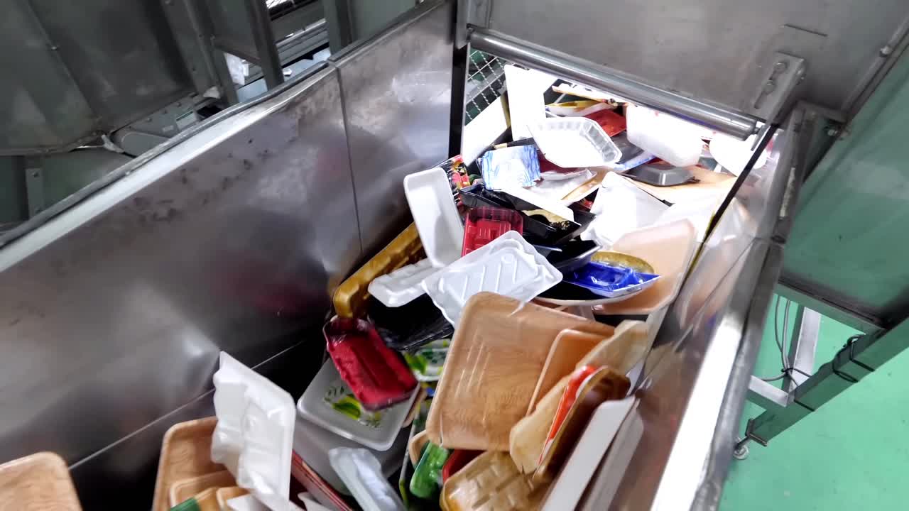Plastic waste is being processed for recycling. Plastic boxes, foam, and paper packaging are transported along the sorting line on a conveyor belt.