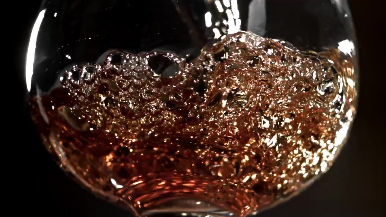 Versamento al rallentatore di liquido ambrato dorato in un bicchiere