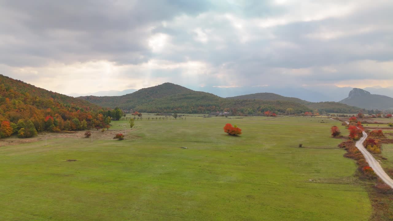 Aerial drone footage showing a wide autumn meadow on a plateau surrounded by mountains in Lika, Croatia. Warm golden tones, colorful trees, and calm natural scenery in soft light