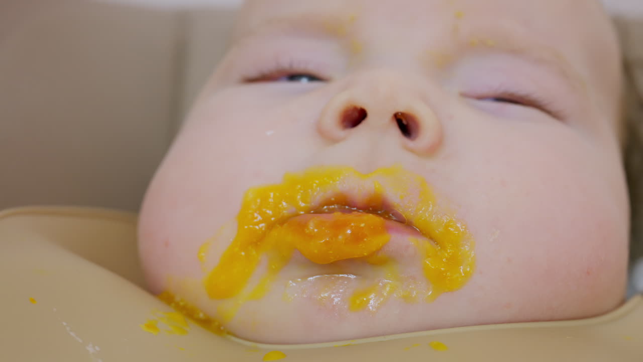 スプーンで離乳食を与えられている赤ちゃんのクローズアップ。顔の細部と穏やかな表情が見える。