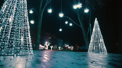 steadicam cinemática filmada en modo bajo de iluminación navideña en la noche, algunas luces colgadas en los árboles y pinos blancos falsos con luces led