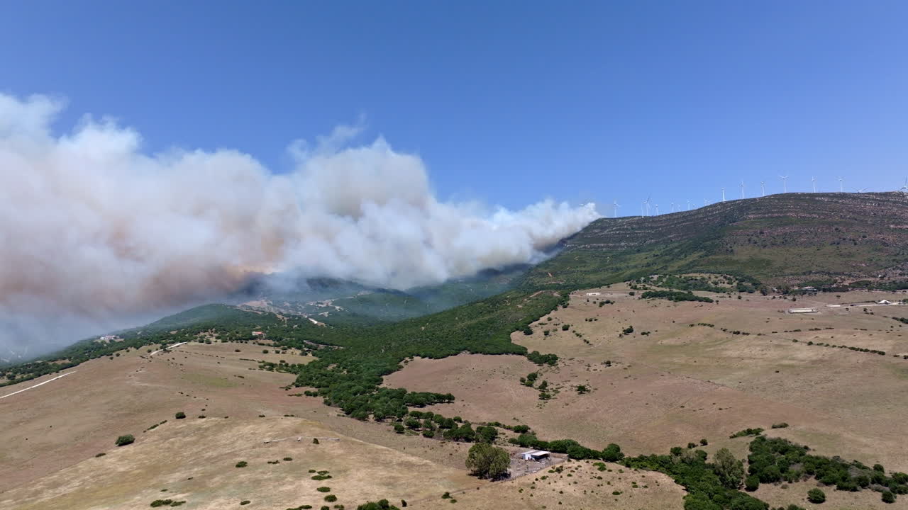 Wildfire engulfs the mountain peak of Valdevaqueros in Tarifa, Spain. Flames rage to the summit due to extreme heat and dryness, creating a dramatic and destructive scene.