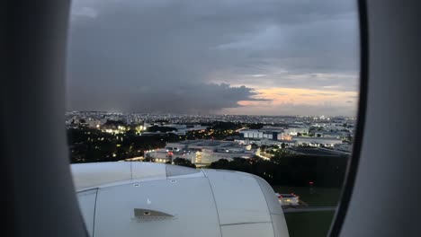 aerial view through airplane window of city buildings in singapore at sunset with thunder lightning and overcast