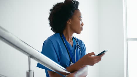 female doctor or nurse browsing on mobile phone on stairs in hospital