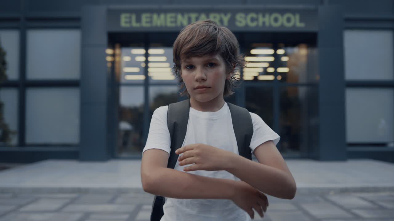 en primer plano, un niño lindo de la escuela de pie con las manos cruzadas. un alumno posando en el patio de la escuela.