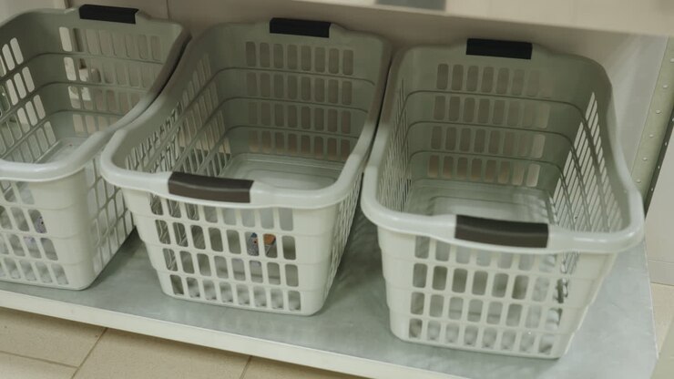 High angle view of white laundry baskets neatly arranged on metal shelf inside laundry facility, showcasing clean empty plastic containers used for organizing or carrying clothes in service environment