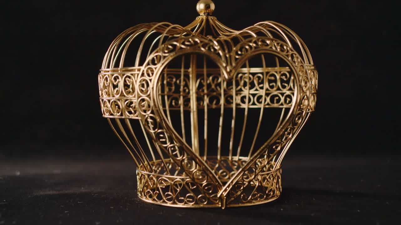 Die Kamera fährt näher an einen goldenen Metallherz-Käfig auf einem Studiotisch heran und zeigt Filigran.