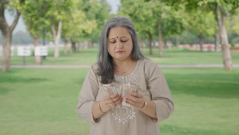 una anciana india contando dinero en el parque.