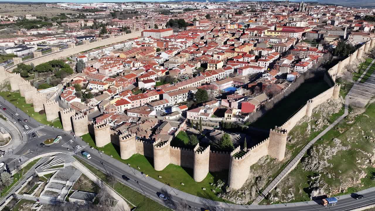o voo de scramble em ascensão, observando a cidade murada medieval de ávila, patrimônio da humanidade da unesco, vendo suas casas dentro da muralha e uma estrada com carros em circulação em um dia ensolarado de inverno na espanha.