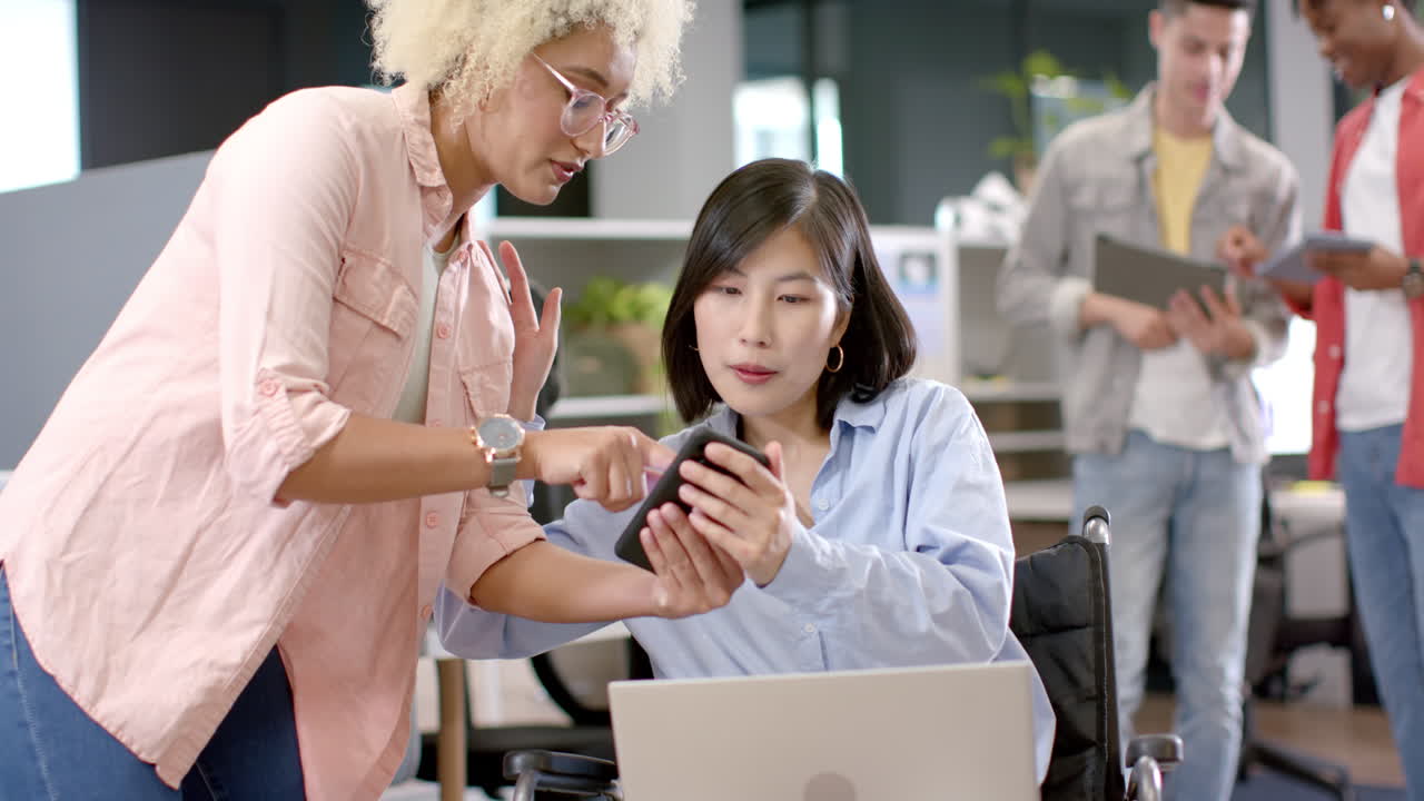 Collaborating in office, colleagues discussing work on smartphone and laptop
