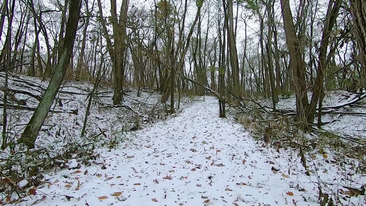 POV from the front of off road vehicle while driving across a  grassy field covered with a light snow on a cloudy winter afternoon, ending in a wooded area