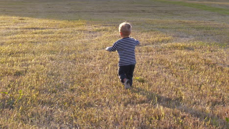 toddler boy runs through harvested field, slow motion shot