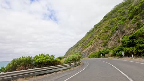 a car travels along the picturesque great ocean road, flanked by cliffs and ocean under a partly cloudy sky
