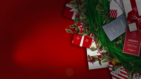 red particles falling over christmas wreath decoration and gifts against red background