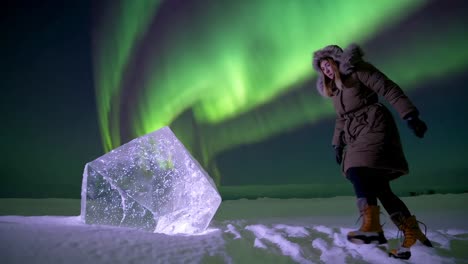 woman exploring a massive ice block under the northern lights