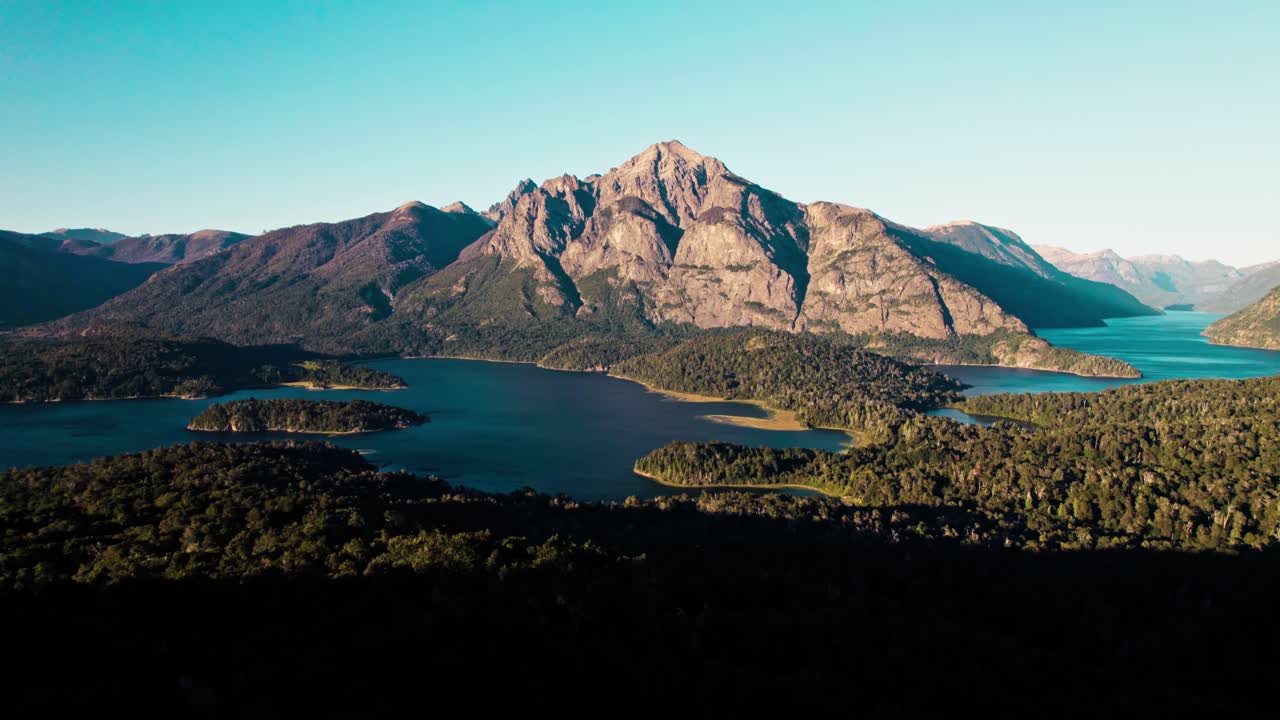 Ampia ripresa aerea che cattura la vasta scala del paesaggio patagonico. Presenta un'imponente vetta montana dominante, baie lacustri interconnesse e rigogliose foreste verde scuro che ricoprono le pendici inferiori.