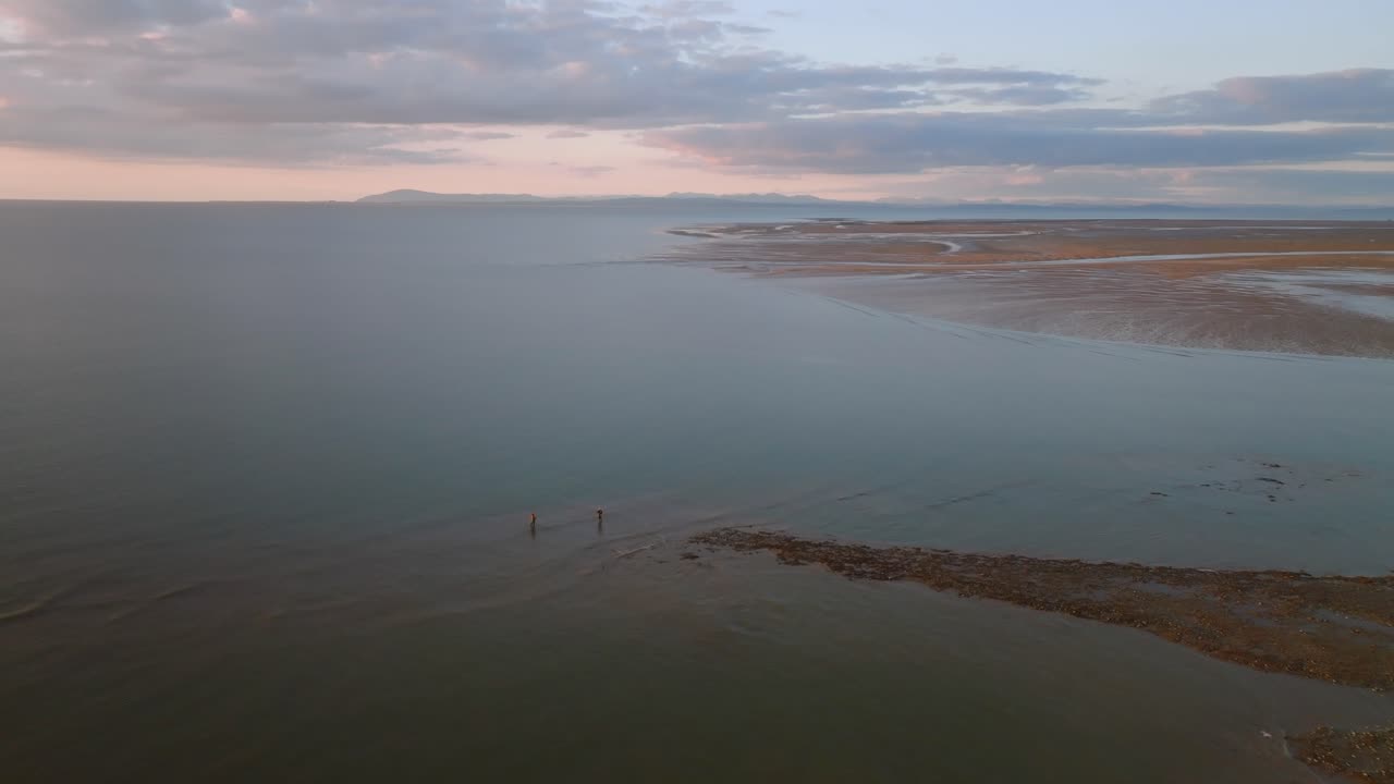 Two Lone Fishermen Standing On The Tide Line Of The Irish Sea At Low Tide At Sunset. Fleetwood, Lancashire, UK
