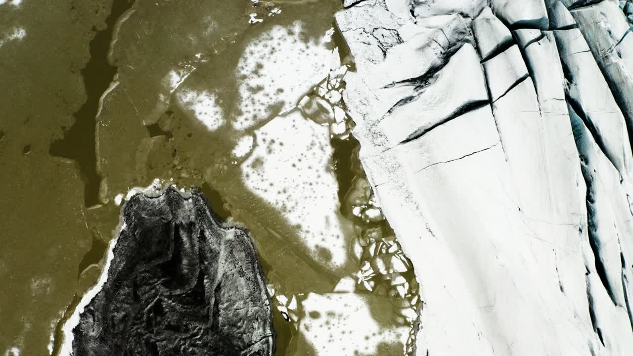 Aerial top-down shot capturing icy meltwater, frozen textures, and rugged glacier formations in Svínafellsjökull Glacier, Iceland.