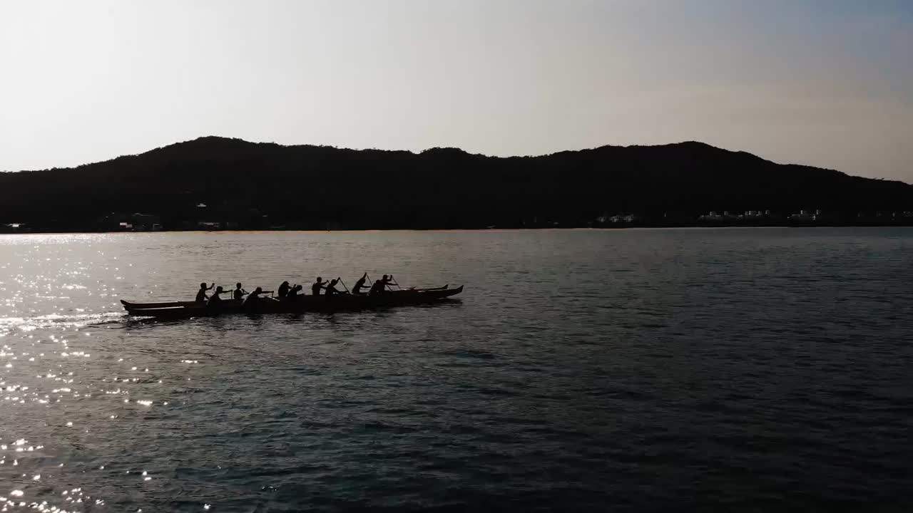 Cinematic aerial orbit shot around kayak team paddling on Brazilian coastline in summer