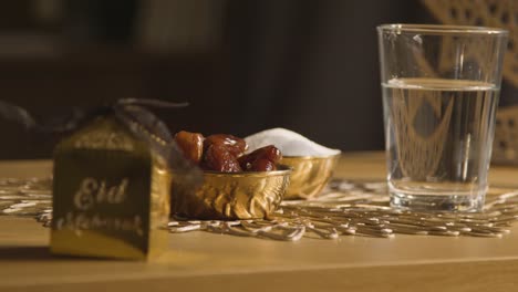 tazón de dátiles con vaso de agua y cajas de regalo sobre la mesa en un hogar musulmán celebrando el eid 1