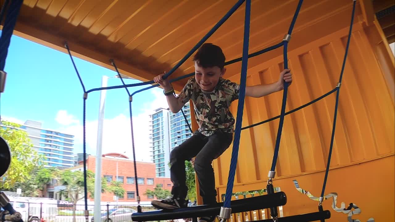 un niño feliz se acerca y sube a través de un columpio de cuerda en un patio de recreo industrial