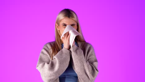 Caucasian-blonde-young-Woman-blows-her-nose-with-tissue-sneezing-in-infinite-pink-chroma-background-studio-portrait-shot-in-casual-clothes