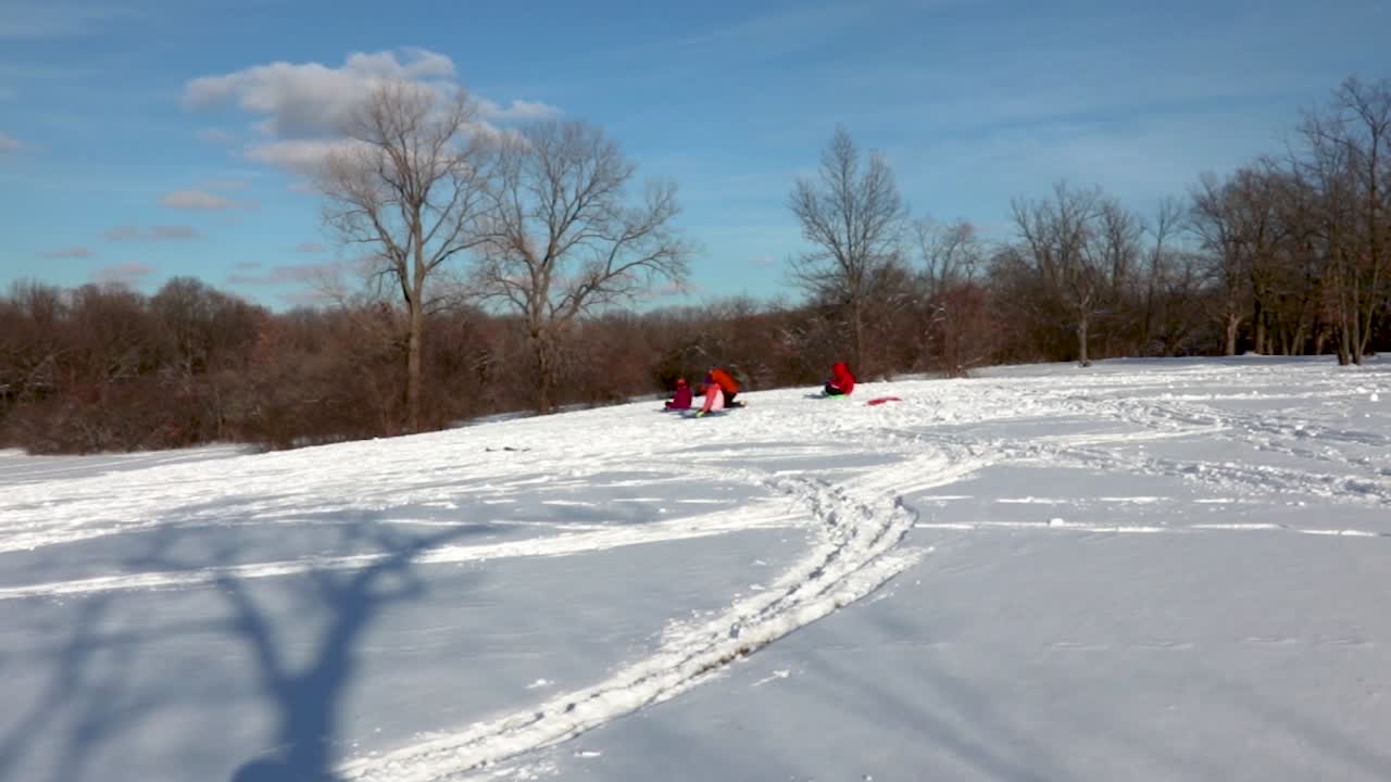 un padre de alto rendimiento empuja a su hijo menor cuesta abajo en un trineo, lo que indica lo bien que se divierten juntos como familia