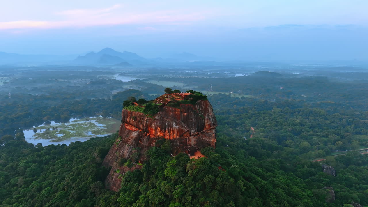 Panning footage around brown mountain standing in lush greenery. Aerial perspective on Sigiriya rock fortress in Sri Lanka.