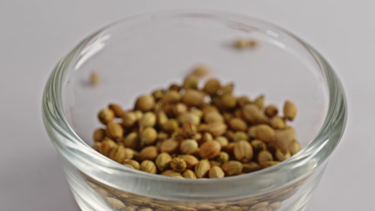 Coriander seeds falling in small glass bowl, 4k, stable shot