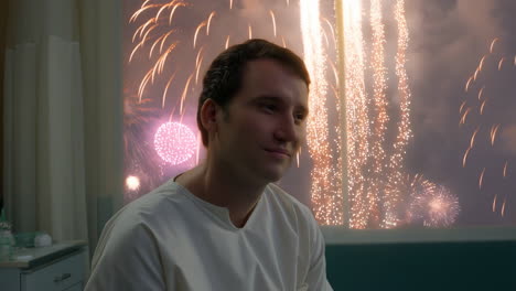 man in hospital gown watches fireworks from his room