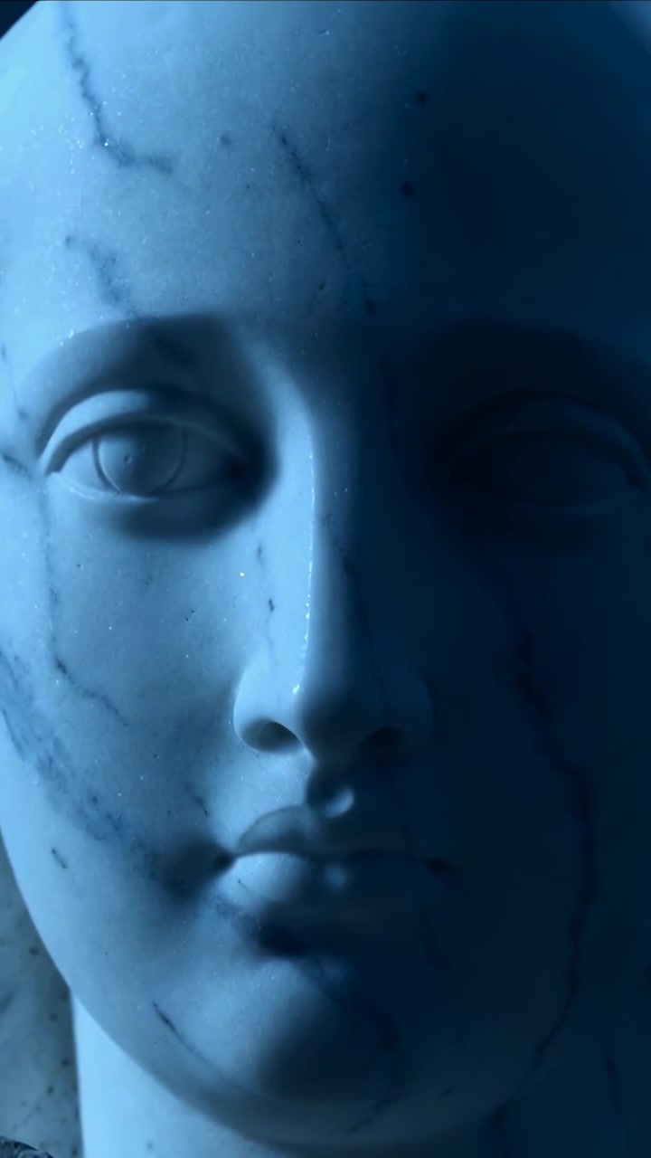 Video verticale: Telecamera che panoramica su un busto di marmo e la sua base in uno studio illuminato di blu, rivelando le venature.