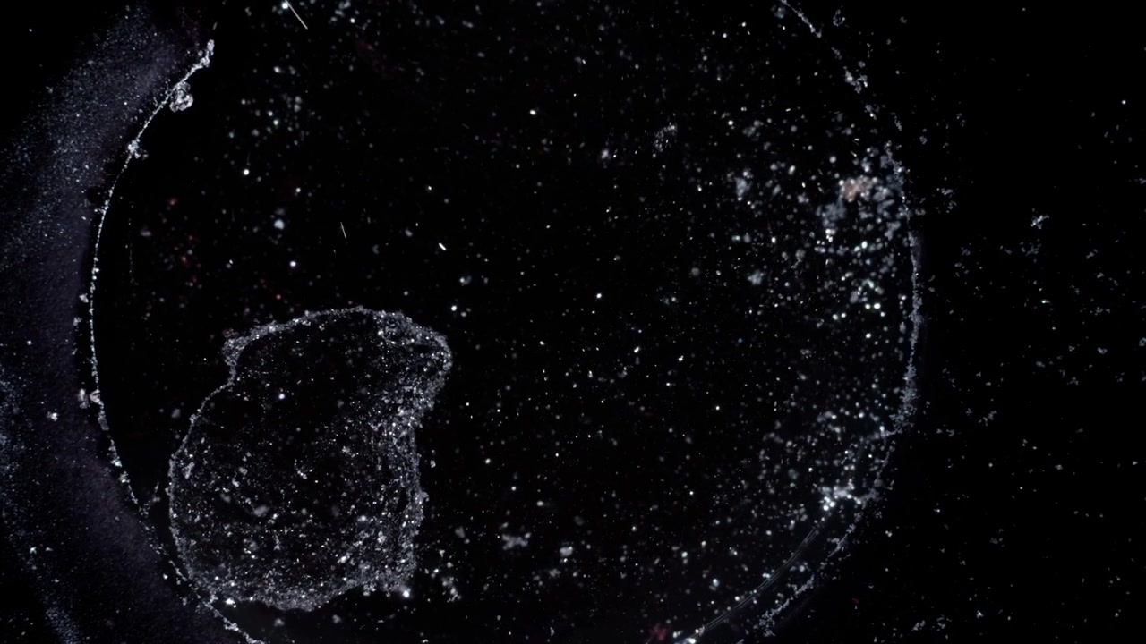 Top-down macro view of silver particles swirling in black liquid, mimicking a deep space galaxy with stars. Cinematic high-contrast abstract texture for science and meditation visuals.
