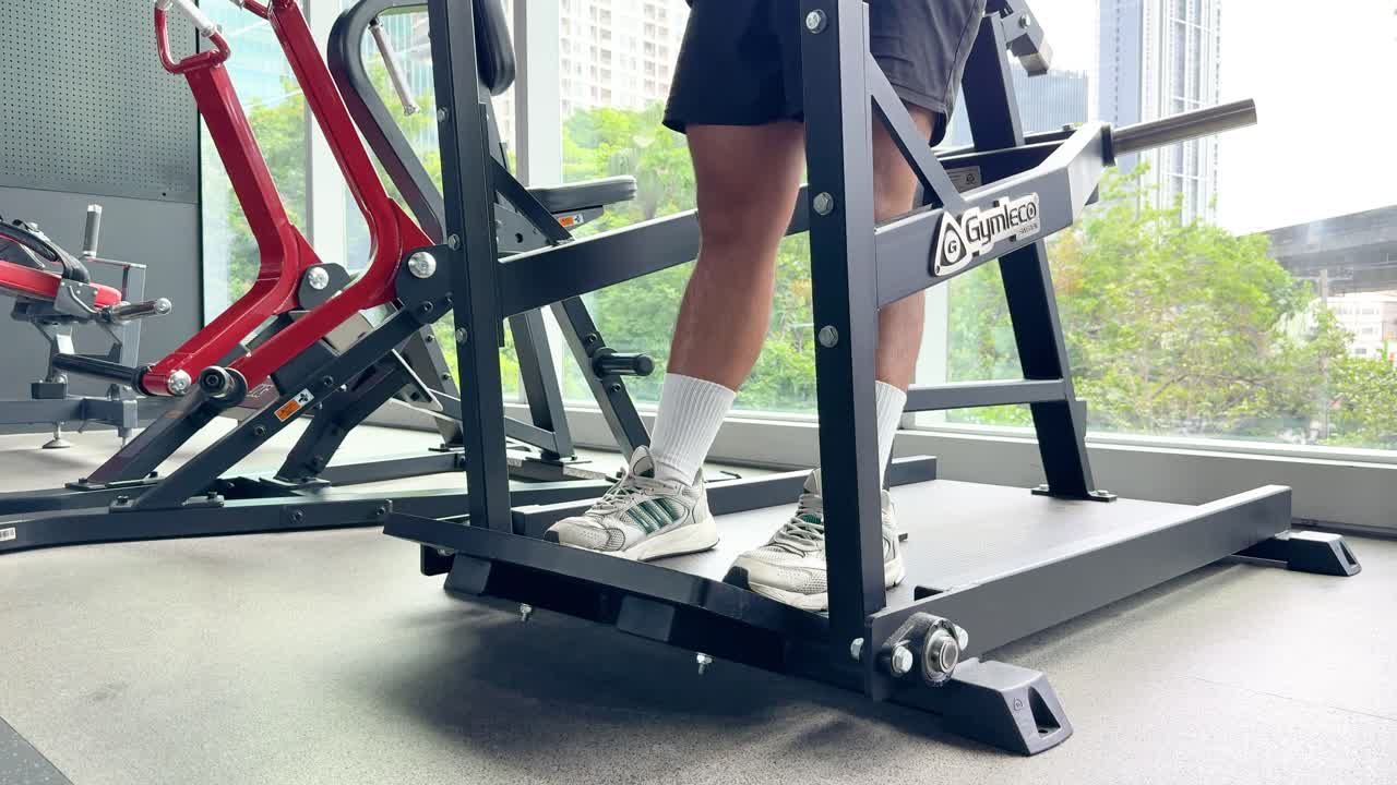 Athlete lifts weights on Smith machine in bright gym with city view and natural daylight