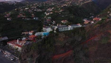 a circling drone shot of a hotel on top of the steep cliff in ponta do sol in madeira during the last rays of sunshine from the sunset