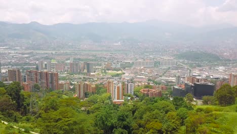 Easy-and-slow-aerial-shot-of-Medellin-skyscrapers-in-city-center-with-green-grass-hills