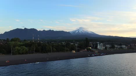 aerial approach towards shore of villarrica lake in pucon, chile with towering villarrica volcano in background