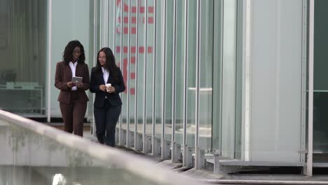 smiling businesswomen looking at tablet during stroll