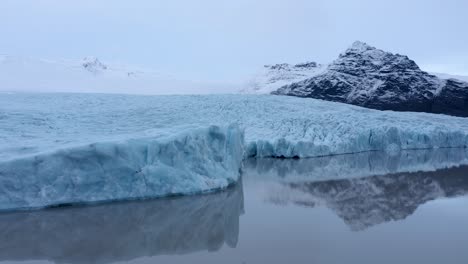 vuelo de drones de ángulo bajo sobre la laguna glaciar en islandia y montañas nevadas en segundo plano