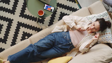 woman in headphones resting on sofa and listening to music