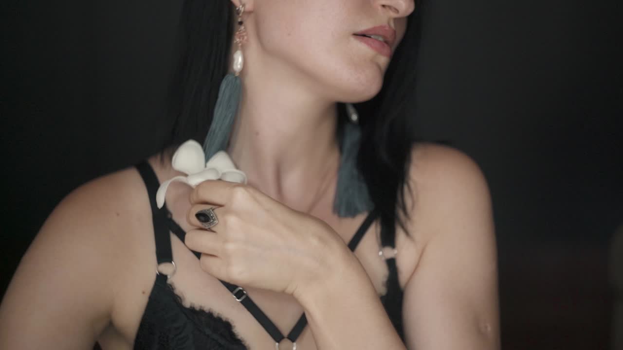 Donna femminile che si tocca le labbra con un bellissimo fiore, primo piano su sfondo nero