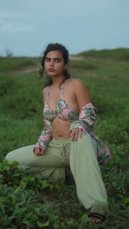 woman in a tropical print bikini top stands outdoors with a thoughtful expression, vertical shot