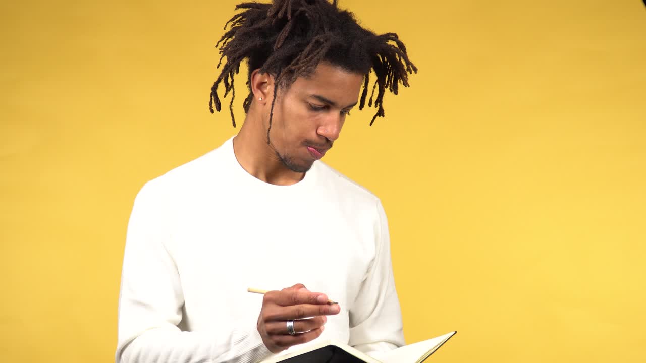 Young black male student in white sweater opens notebook and starts to wright