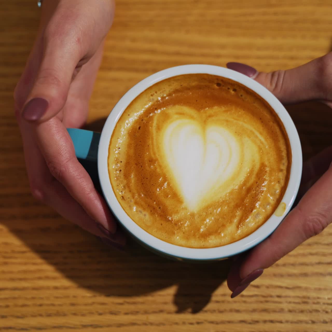 Serving a cup of hot drink. Heart design from milk on coffee. Cup of coffee with latte art in a form of a heart on a wooden background. Close-up.