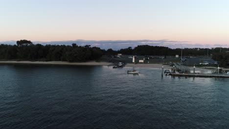 Aerial-view-of-boat-waiting-at-dock-to-be-loaded-as-a-jets-is-being-loaded-onto-boat-ramp-at-sunset-in-Southport-Gold-Coast-QLD-Australia