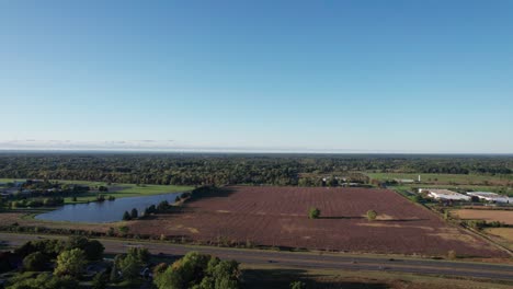 Hermoso-Dron-Aéreo-Que-Se-Mueve-Hacia-Adelante-Sobre-Grandes-Tierras-De-Cultivo-Junto-A-Un-Lago-En-Una-Tarde-Otoñal