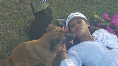 una chica asiática con vestido blanco acostada en un prado rodeada de sus dos perros, el plano constante muestra a la chica acariciando a uno de los perros el estado de ánimo está relajado, y los animales están tranquilos