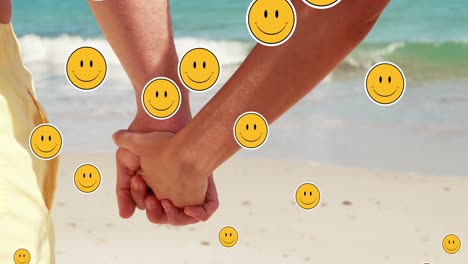 Emoji-Mit-Mehreren-Lächelnden-Gesichtern,-Das-Gegen-Den-Mittelteil-Eines-Paares-Schwebt,-Das-Sich-Am-Strand-An-Den-Händen-Hält