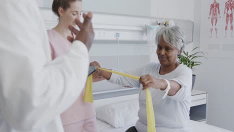 un médico masculino diverso hablando con una fisioterapeuta femenina y una paciente femenina anciana feliz, en cámara lenta.